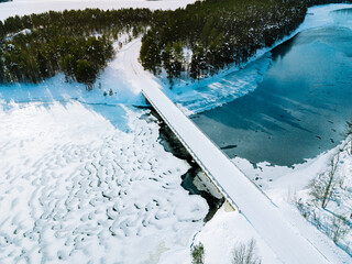 Aerial view of snow winter river with bridge and green forest