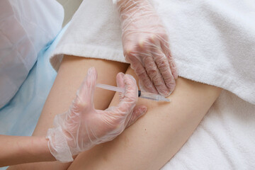 Cosmetologist conducts a session of mesotherapy making an injection in the patient's leg