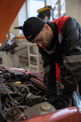 Fototapeta na wymiar Vertical portrait of male mechanic looking under hood while repairing car in auto shop