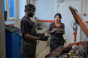 Side view portrait of two mechanics repairing car in auto shop with focus on African-American worker inspecting engine, copy space