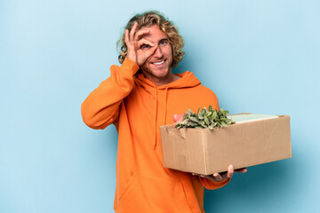 Young caucasian man making a move while picking up a box full of things isolated on blue background...