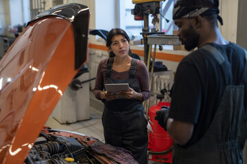 Waist up portrait of female mechanic using digital tablet while inspecting car in auto repair workshop