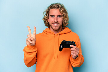 Young caucasian man playing with a video game controller isolated on blue background showing number two with fingers.