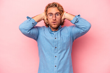 Young caucasian man isolated on pink background covering ears with hands trying not to hear too loud sound.