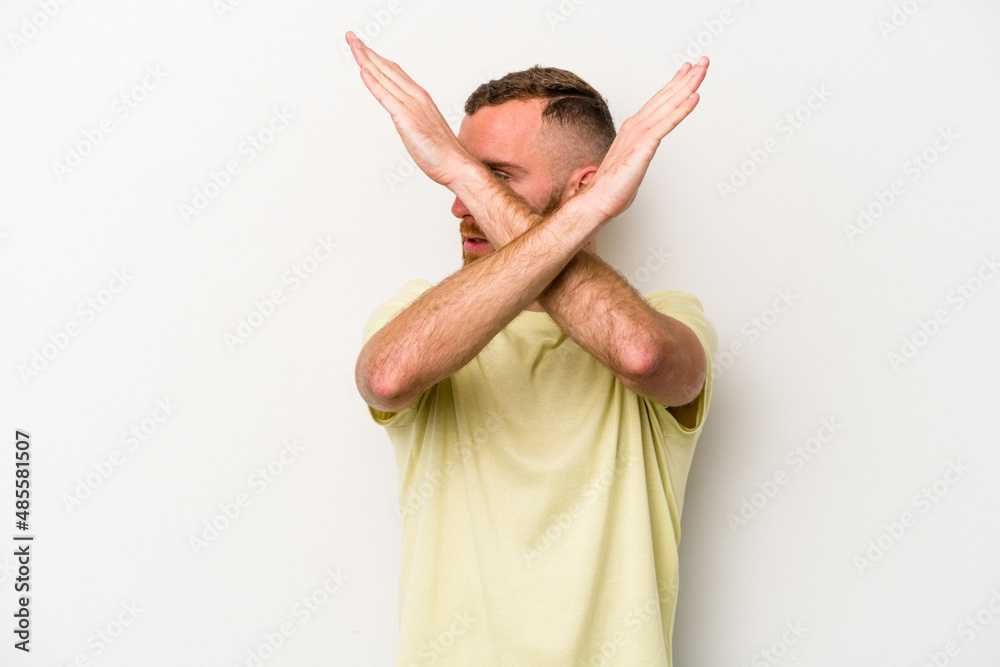 Wall mural young caucasian man isolated on white background keeping two arms crossed, denial concept.