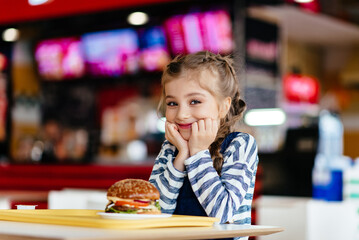 Cute little girl eating fast food hamburger in cafe