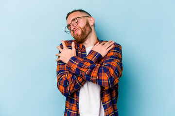 Young caucasian man isolated on blue background hugs, smiling carefree and happy.