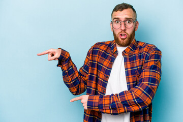 Young caucasian man isolated on blue background shocked pointing with index fingers to a copy space.