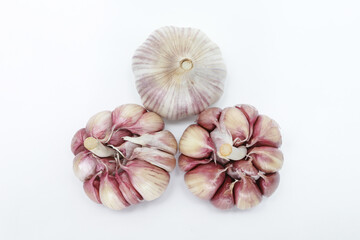 Three heads of garlic (Allium sativum), seen from above, with their units still in the bulb, one with the skin and two without, on a neutral background