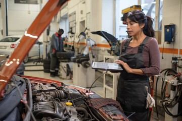 Side view portrait of young female mechanic using laptop while inspecting vehicle in car repair...