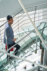 Smiling man with baggage and cellphone going up stairs