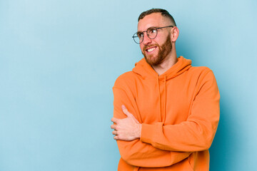 Young caucasian man isolated on blue background smiling confident with crossed arms.