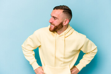 Fototapeta premium Young caucasian man isolated on blue background laughs happily and has fun keeping hands on stomach.
