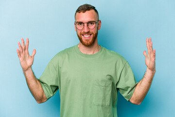 Naklejka premium Young caucasian man isolated on blue background holding something little with forefingers, smiling and confident.