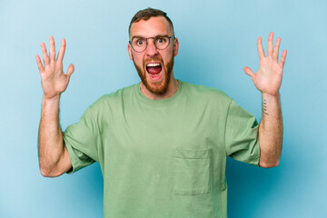 Young caucasian man isolated on blue background receiving a pleasant surprise, excited and raising hands.