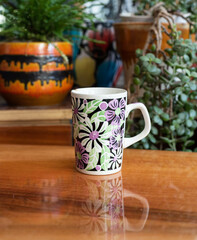 Mid-century modern porcelain cup with spray painted pattern on a wooden table, with plants in the background