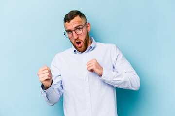 Young caucasian man isolated on blue background surprised pointing with finger, smiling broadly.