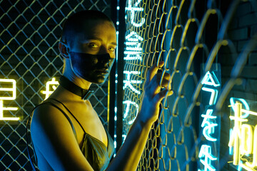Portrait of cyberpunk woman with black paint on her face standing near the bars and looking at...
