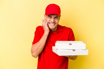 Young delivery caucasian man holding pizzas isolated on yellow background covering ears with hands.