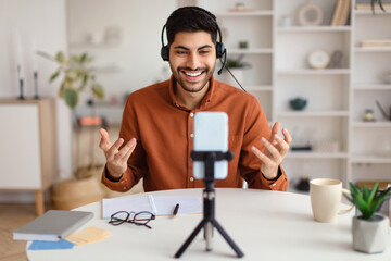 Arab man having videocall using cellphone on tripod and talking