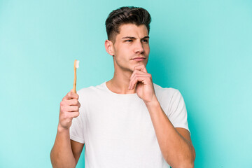 Young caucasian man brushing teeth isolated on white background looking sideways with doubtful and skeptical expression. - obrazy, fototapety, plakaty