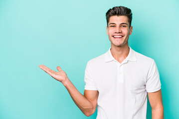 Young caucasian man isolated on blue background showing a copy space on a palm and holding another hand on waist.