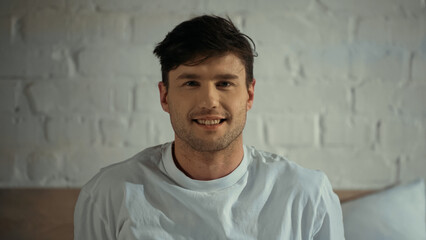 man in white t-shirt smiling at camera in bedroom