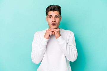 Young caucasian man isolated on blue background praying for luck, amazed and opening mouth looking to front.