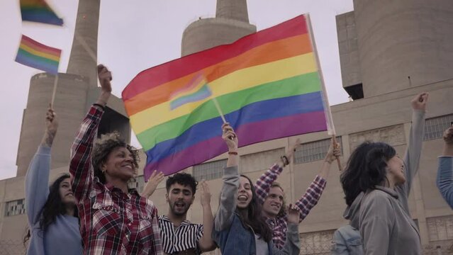Protestors waving a rainbow coloured flag at a street parade. People attending a gay pride march in the city.