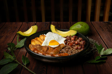Still life of bandeja paisa, typical Colombian food, from antioquia, with beans, eggs, rice, pork rinds, avocado and chorizo ​​in plate on brown table