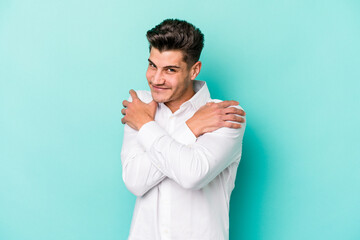 Young caucasian man isolated on blue background hugs, smiling carefree and happy.