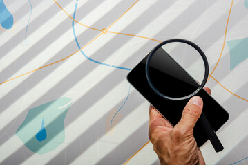 Detective hand holding magnifying glass and smartphone in front of city map