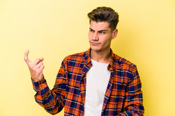Naklejka premium Young caucasian man isolated on yellow background pointing with finger at you as if inviting come closer.
