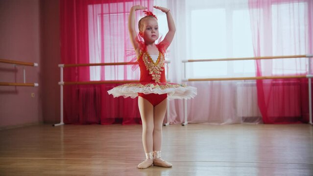 A little girl in red dress stands in ballet position