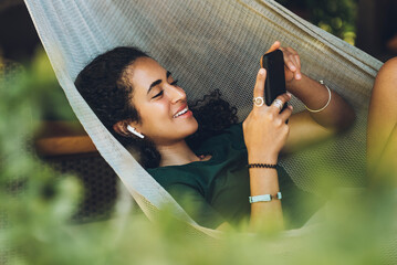 Beautiful brunette woman with laughing hair resting in a hammock with her cell phone and wireless...