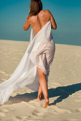 Back view of naked woman in white pareo walking on beach on sunny day