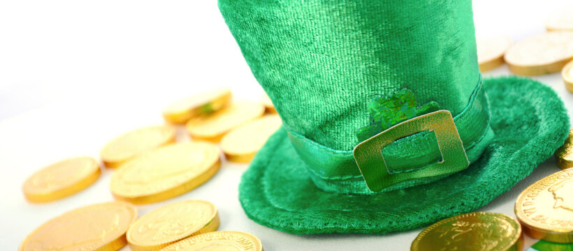 St Patricks Day leprechaun hat with chocolate gold covered coins on white wood backround. Sized to fit popular social media and web banner.