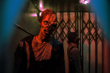 Waist up shot of male zombie with scary face in dark hallway lit by red light, copy space