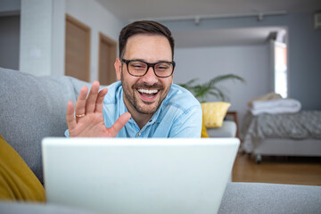 A happy mature man relaxes on the couch while making video calls using a laptop at home. A man lies on a sofa and makes a video call. A smiling Middle Eastern businessman makes an online video. 