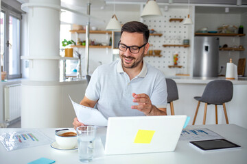 A young serious professional businessman, a focused student who wears glasses works on a laptop, learns at a distance using a computer and looks at the screen, watches a seminar webinar