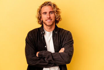 Young caucasian man isolated on yellow background who feels confident, crossing arms with determination.