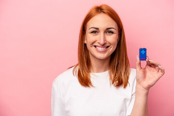 Young caucasian woman holding a batteries isolated on pink background smiling and raising thumb up
