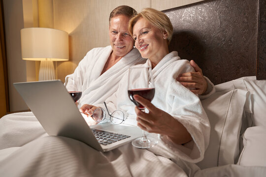 Lovely woman and handsome man looking delighted in hotel bed