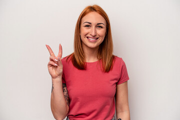 Young caucasian woman isolated on white background showing victory sign and smiling broadly.