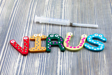 Text VIRUS from letters on a wooden table and a syringe for vaccinations and treatment.