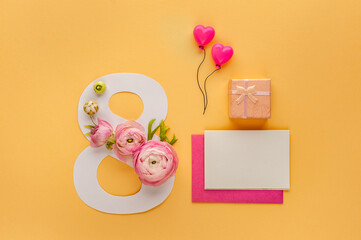 Greeting Card International Women's Day on March 8th. Pink ranunculus decorates the number eight and gift box with bow on orange background.  Card mockup template. Soft focus. Top view.
