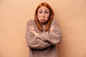 Young caucasian woman isolated on beige background shrugs shoulders and open eyes confused.