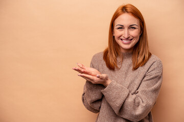 Young caucasian woman isolated on beige background holding a copy space on a palm.