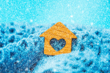 Fototapeta na wymiar Close-up of a small wooden house with a heart lying in a knitted scarf. Blue background with snow. The concept of leasing, home purchase and mortgage