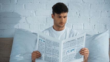 man reading economic news while sitting in bed in morning
